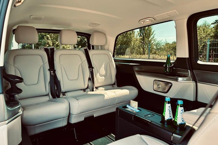 Spacious and luxurious Mercedes V-Class interior with premium leather seats and elegant layout. On-board amenities include bottled water, tissues, USB ports, and ample room for a comfortable ride.